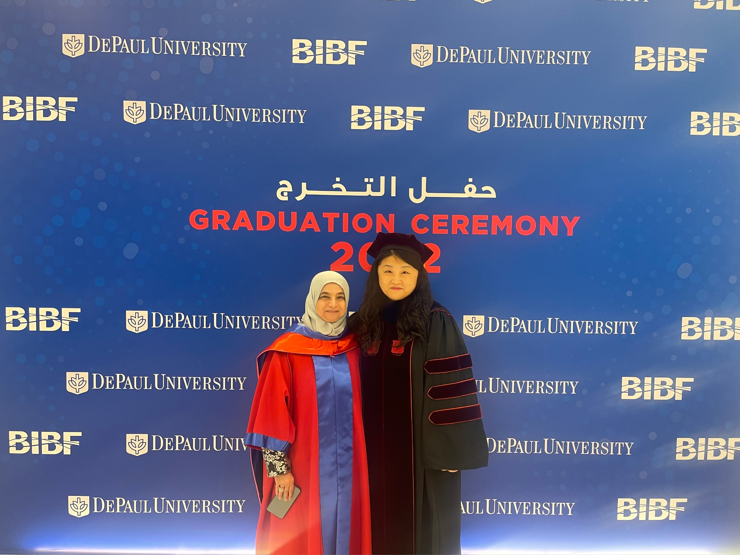 Raja Ali Bucheery and Hui Lin stand before a sign stating Graduation Ceremony 2022 in English and Arabic